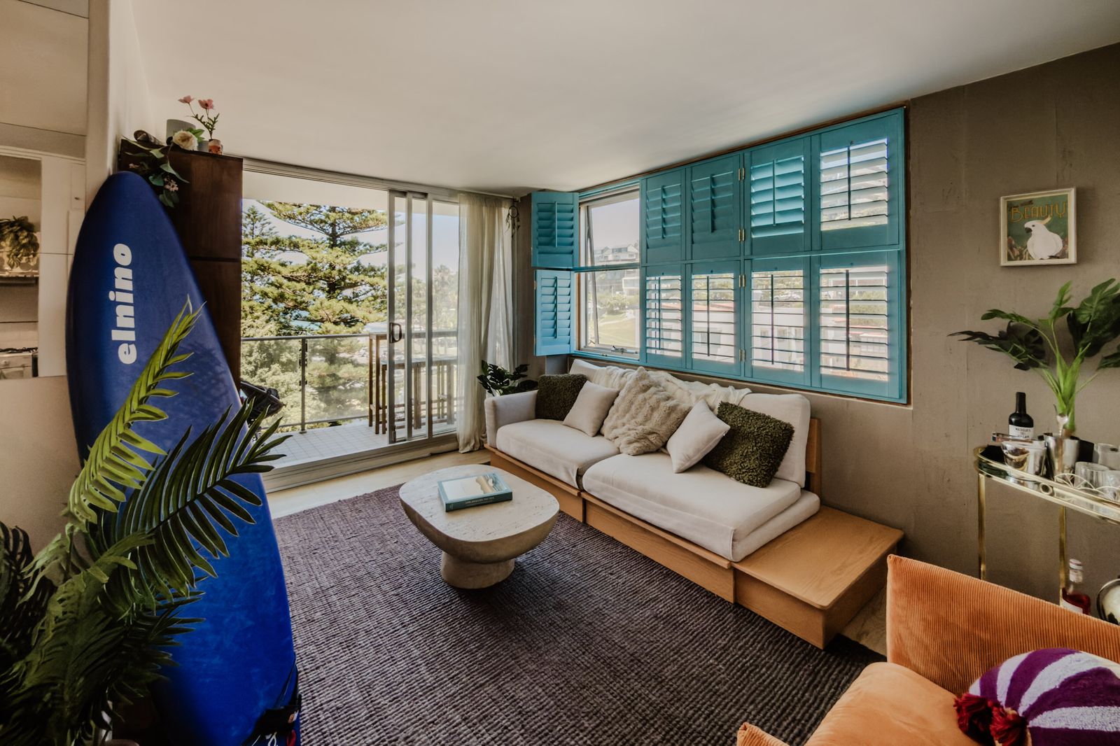 Living room with teal plantation shutters, linen sofa and surfboard